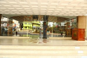 A man standing in a lobby with a tiled floor and a decorative ceiling.