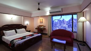 A hotel room with a bed, a desk, a chair, and a large window with a view of palm trees. - Mayura Residency (Chavakkad)