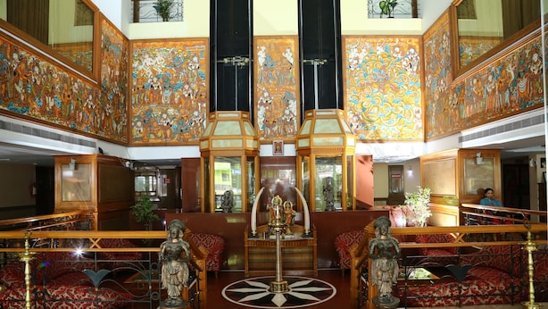 A spacious atrium with ornate wall decorations, a central statue, and a seating area with red patterned cushions. - Mayura Residency (Chavakkad)