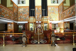 A spacious atrium with ornate wall decorations, a central statue, and a seating area with red patterned cushions.