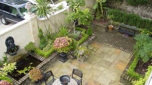 A patio area with a round table and chairs, surrounded by various plants and a stone wall. - The Stephen Williams House (Savannah)