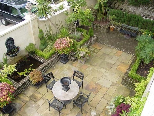 A patio area with a round table and chairs, surrounded by various plants and a stone wall. - The Stephen Williams House (Savannah)