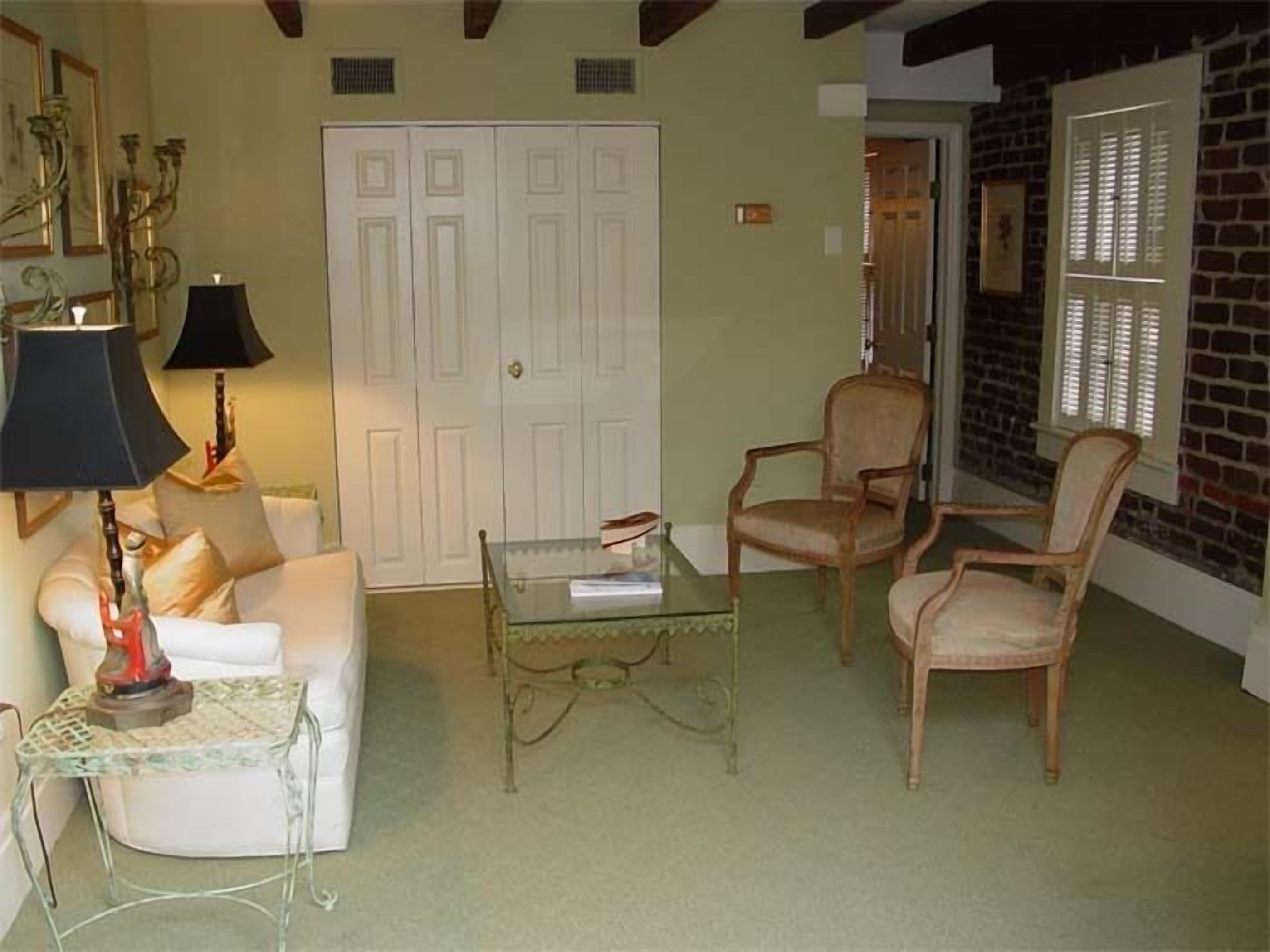 A living room with a white door, two chairs, a glass coffee table, and a lamp.