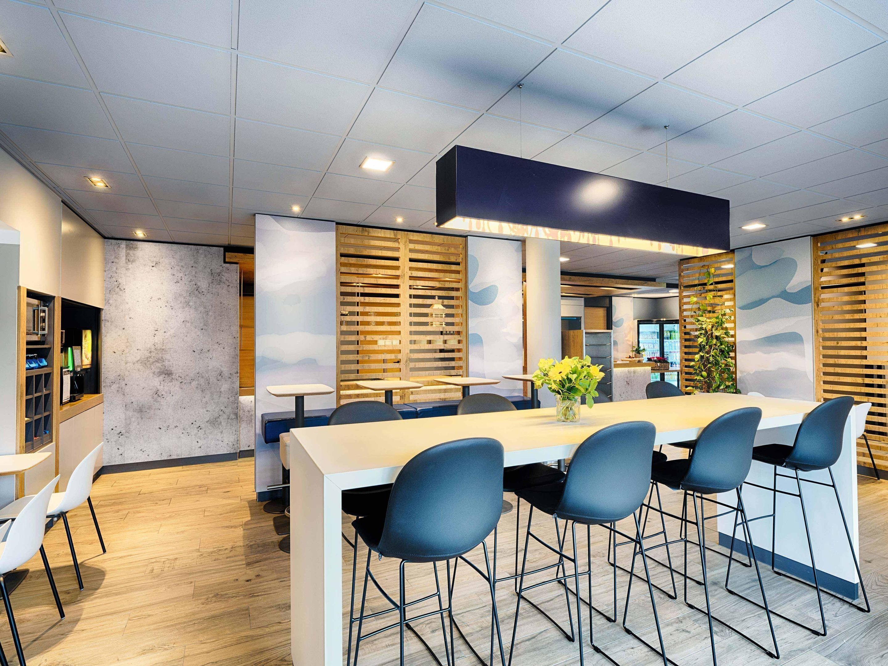 Un espace repas moderne avec une longue table, des chaises bleues et un vase rempli de fleurs jaunes.