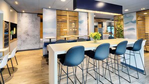 Un espace repas moderne avec une longue table, des chaises bleues et un vase rempli de fleurs jaunes.