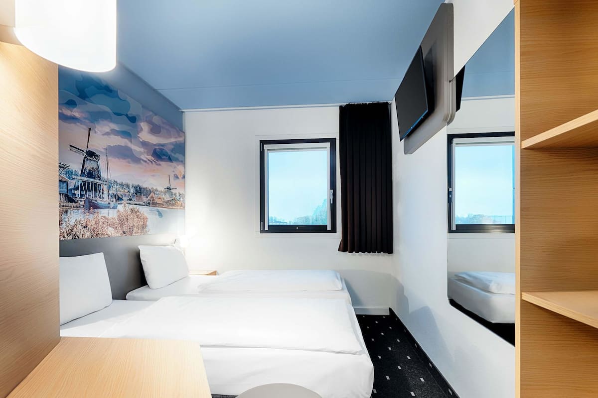 Een hotelkamer met een bed, een bureau, een stoel, een aan de muur bevestigde televisie en een raam met uitzicht op de stad.