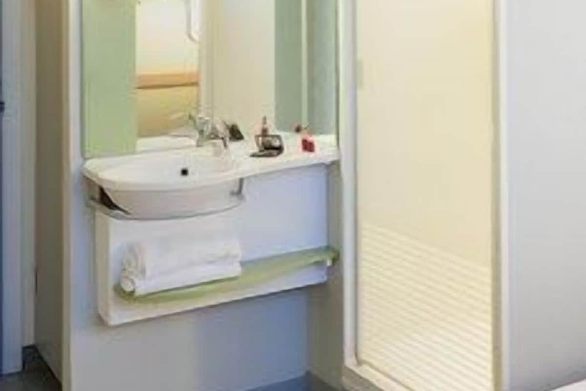Ein Badezimmer mit Waschbecken, Spiegel, Handtuchhalter und Duschkabine.