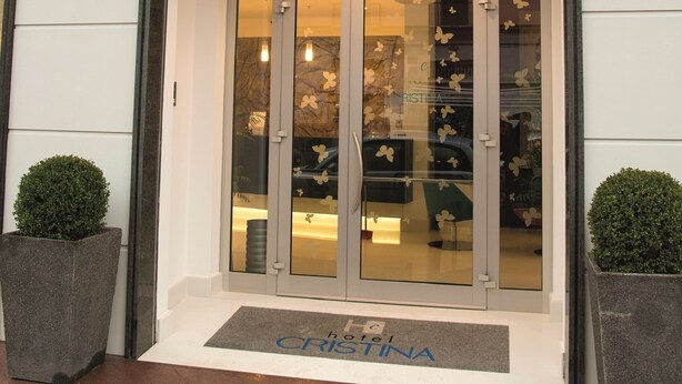 Exterior del Hotel Cristina, con una entrada moderna, puertas de cristal y un cartel sobre la entrada.