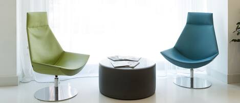 Una habitación moderna con dos sillas, una mesa redonda y un ventanal con cortinas translúcidas.