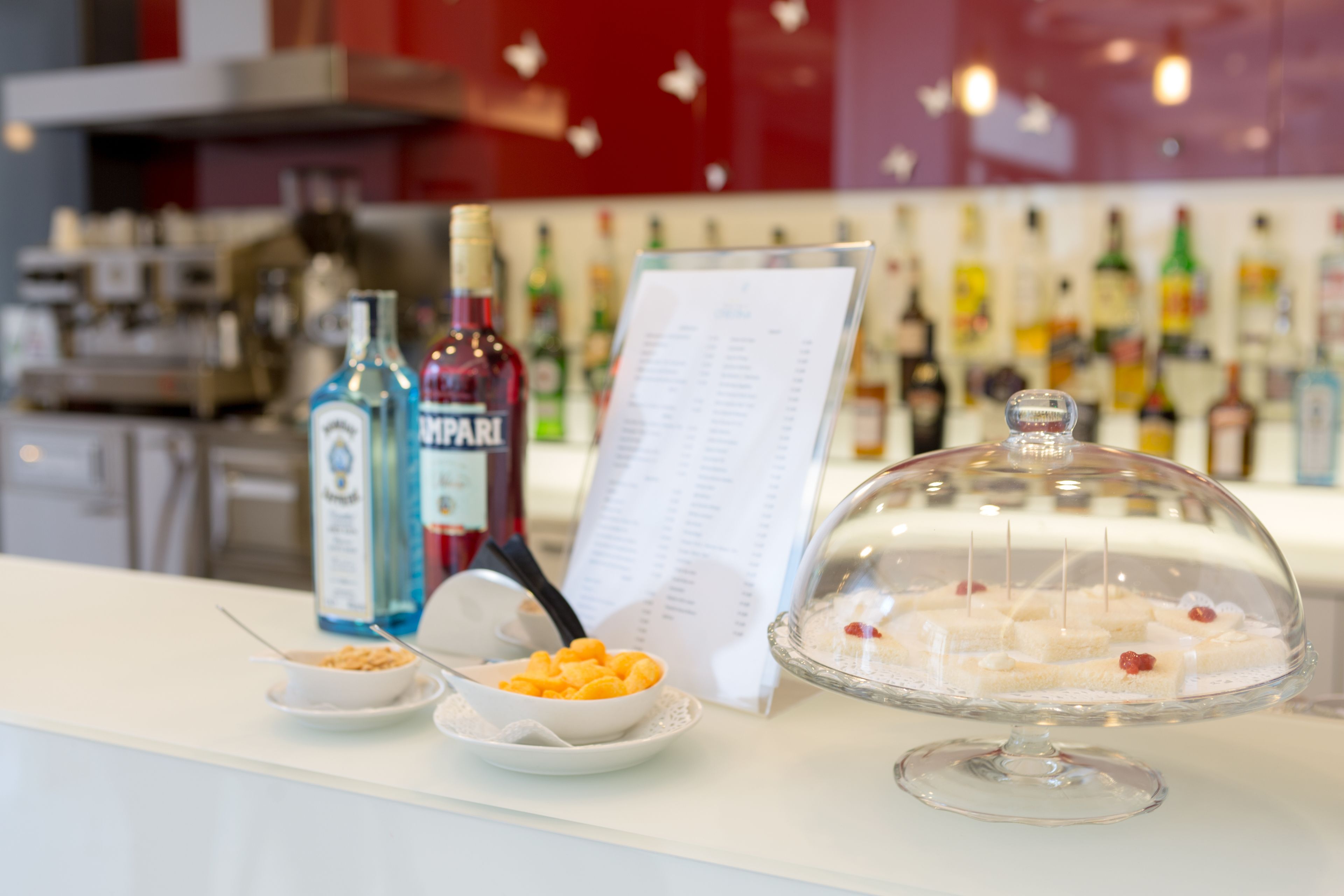 Un espace bar avec un présentoir à menus, une vitrine réfrigérée où sont exposés des desserts, et des bouteilles de spiritueux.