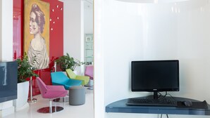 A modern office with a black monitor, keyboard, and mouse on a desk. There are colorful chairs and a large painting on the wall. - Hotel Cristina (Naples)