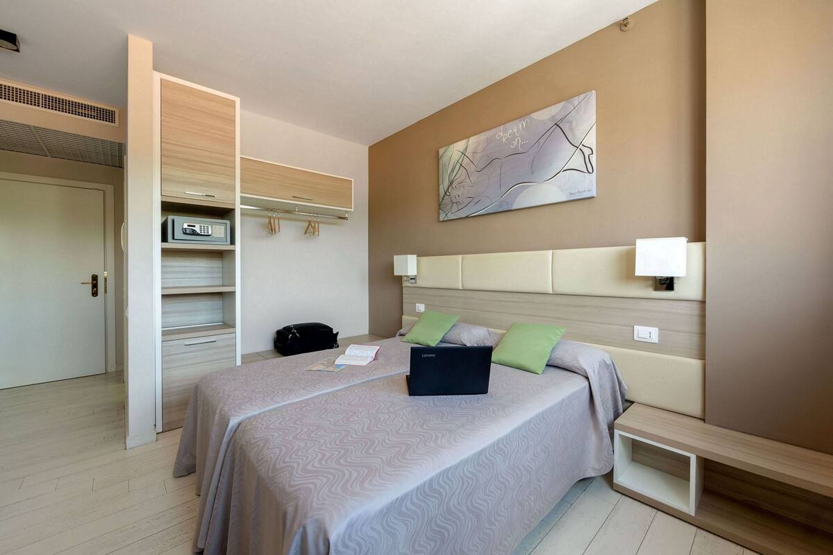 A modern hotel room with a large bed, a built-in wardrobe, a bedside table, and a wall-mounted artwork.