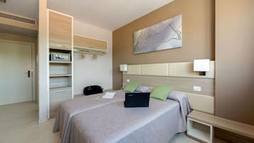 Una habitación de hotel moderna con una cama grande, un armario empotrado, una mesita de noche y una obra de arte colgada en la pared.