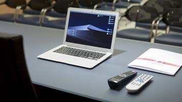 Um laptop sobre uma mesa com um controle remoto e um folheto.