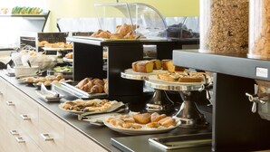 Un bufé con diversas pastas y productos horneados, incluyendo croissants y muffins, expuestos en bandejas y platos.