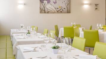 A restaurant with multiple tables, each set with white tablecloths, green chairs, and neatly arranged cutlery and glasses.
