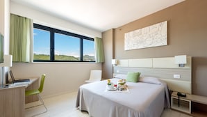 Habitación de hotel moderna con una cama grande, un escritorio con una computadora portátil, una silla verde y vistas al paisaje por la ventana.