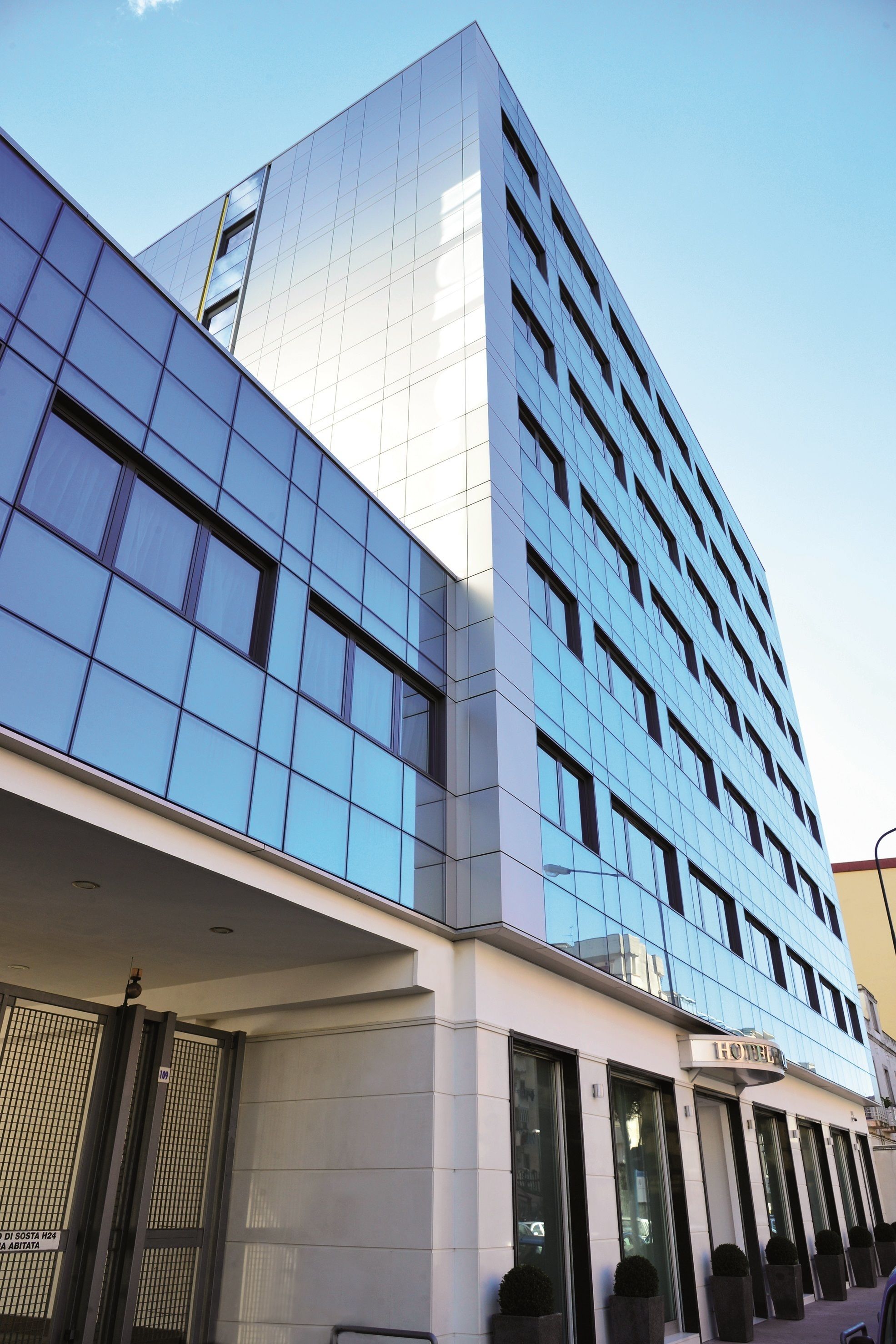 A modern hotel with a reflective glass facade, a prominent entrance with a sign, and a series of windows on the ground floor.