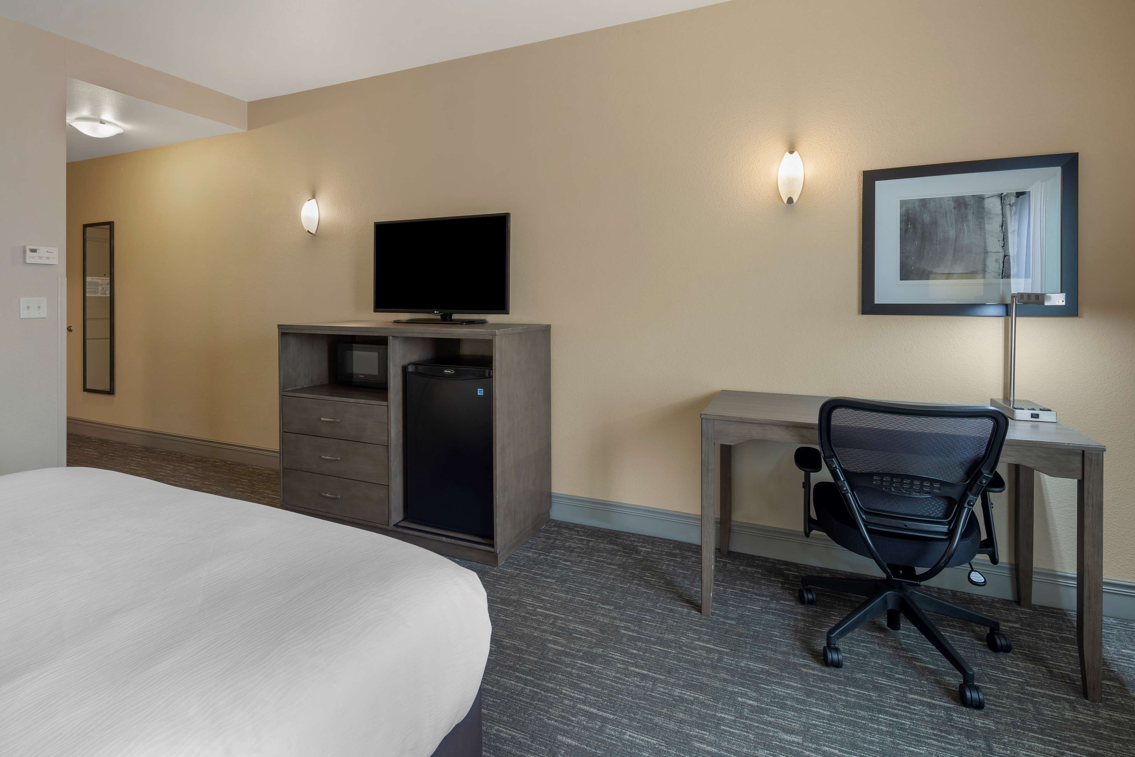 Une chambre d’hôtel comprenant un lit, un bureau avec un ordinateur et une chaise, une télévision et deux appliques murales.