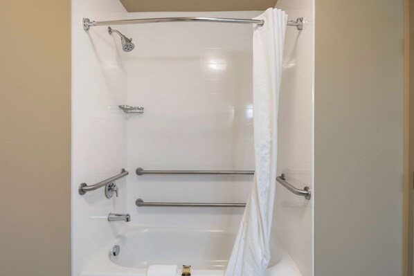 Un baño moderno con ducha a nivel, barras de apoyo y bañera.