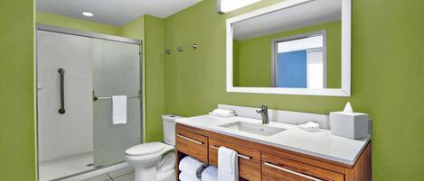 Une salle de bain moderne avec une douche à parois de verre, des toilettes blanches et un meuble-lavabo en bois doté d’un évier et d’un miroir.