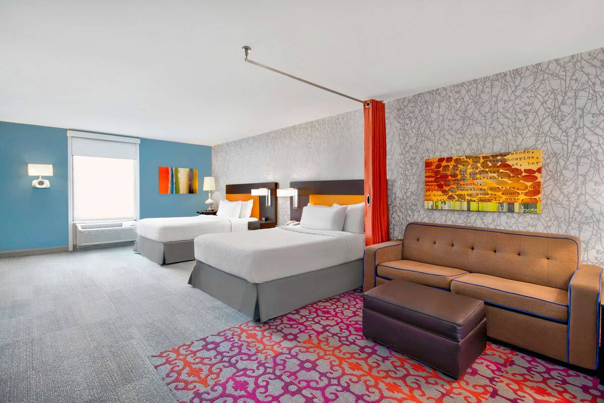 A hotel room with two beds, a sofa, a patterned rug, and a wall art piece.