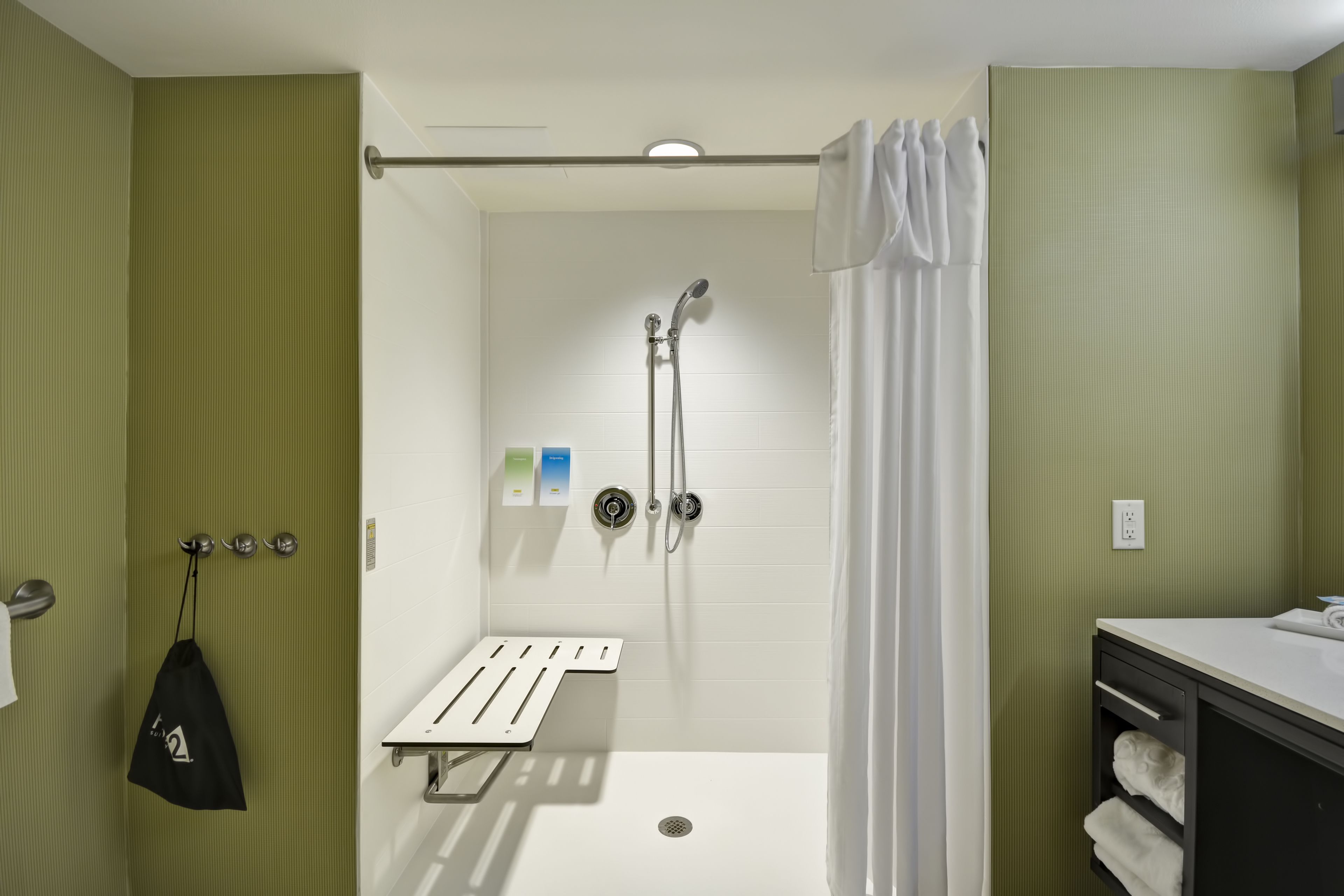 A shower with a white curtain, a towel rack, and a small shelf with toiletries.
