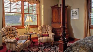 Quarto tradicional com duas poltronas listradas, um armário de madeira e uma janela grande com persianas.
