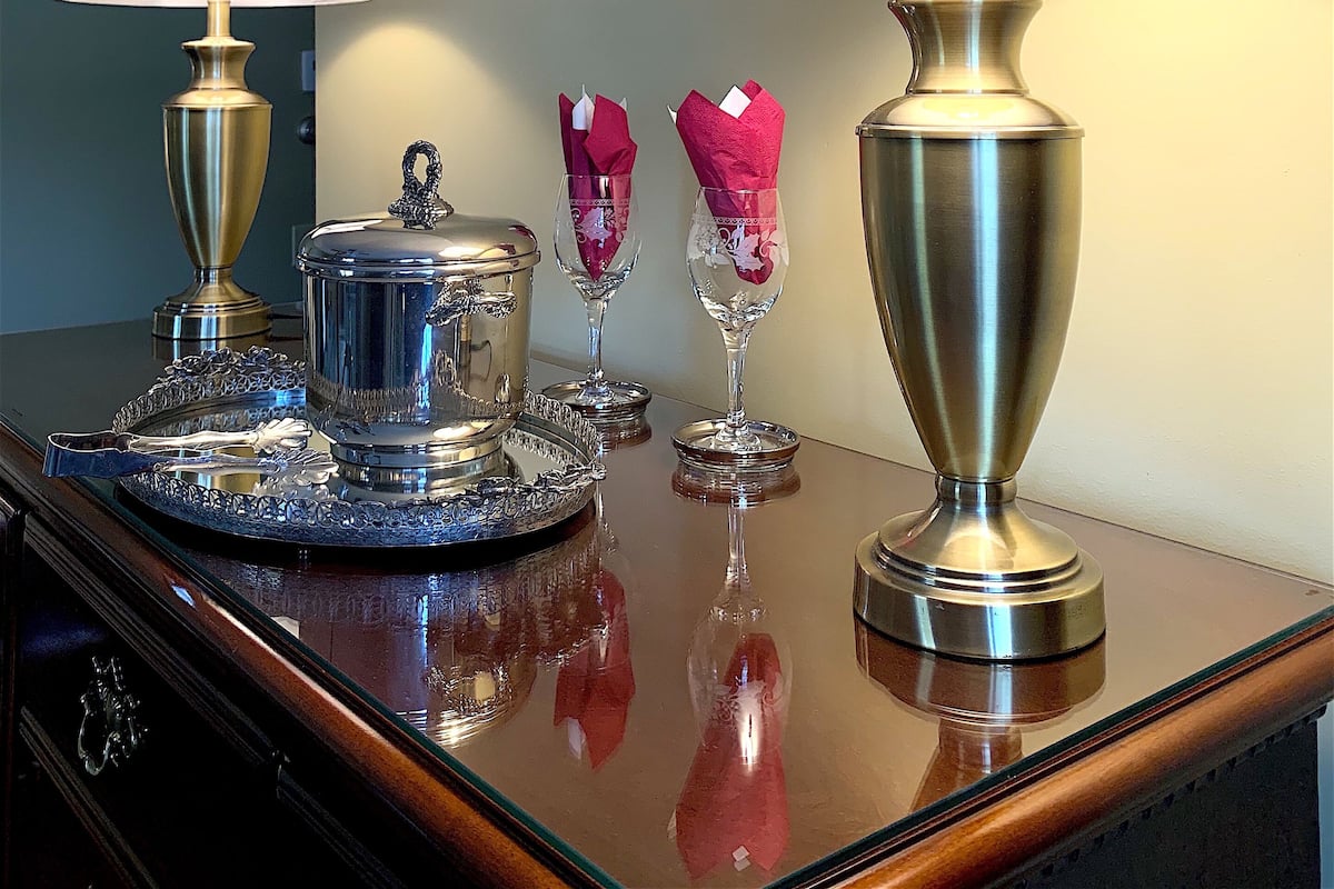 A table with two lamps, a decorative tray, and two wine glasses with napkins.
