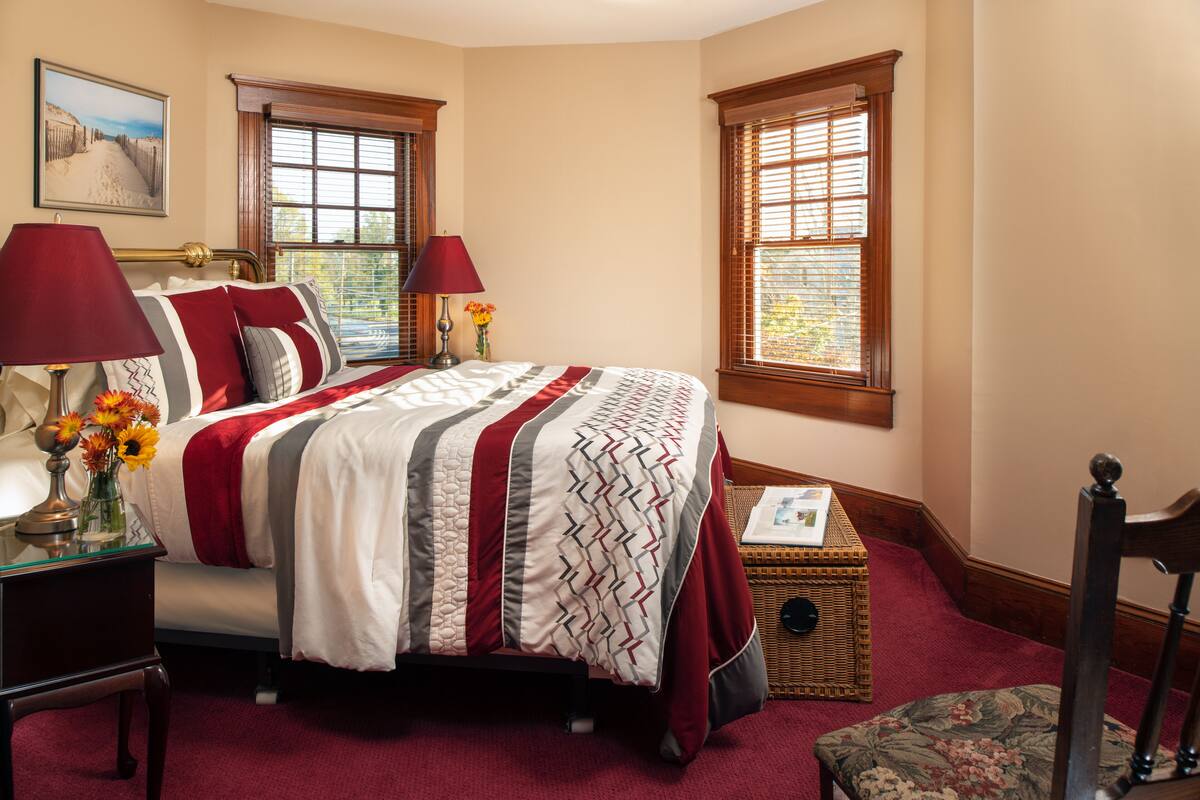 A neatly arranged bedroom with a bed, two bedside tables, a nightstand, a chair, and a small table with a lamp.