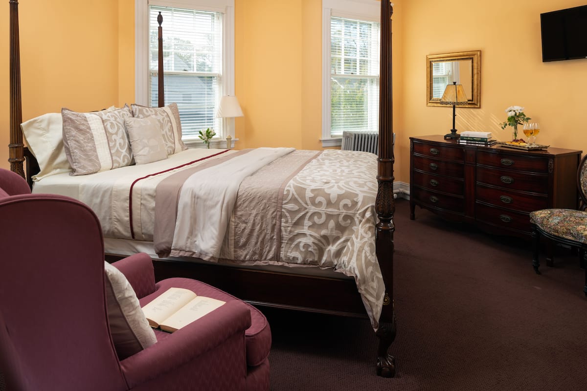 A bedroom with a four-poster bed, a dresser, a chair, and a television on the wall.