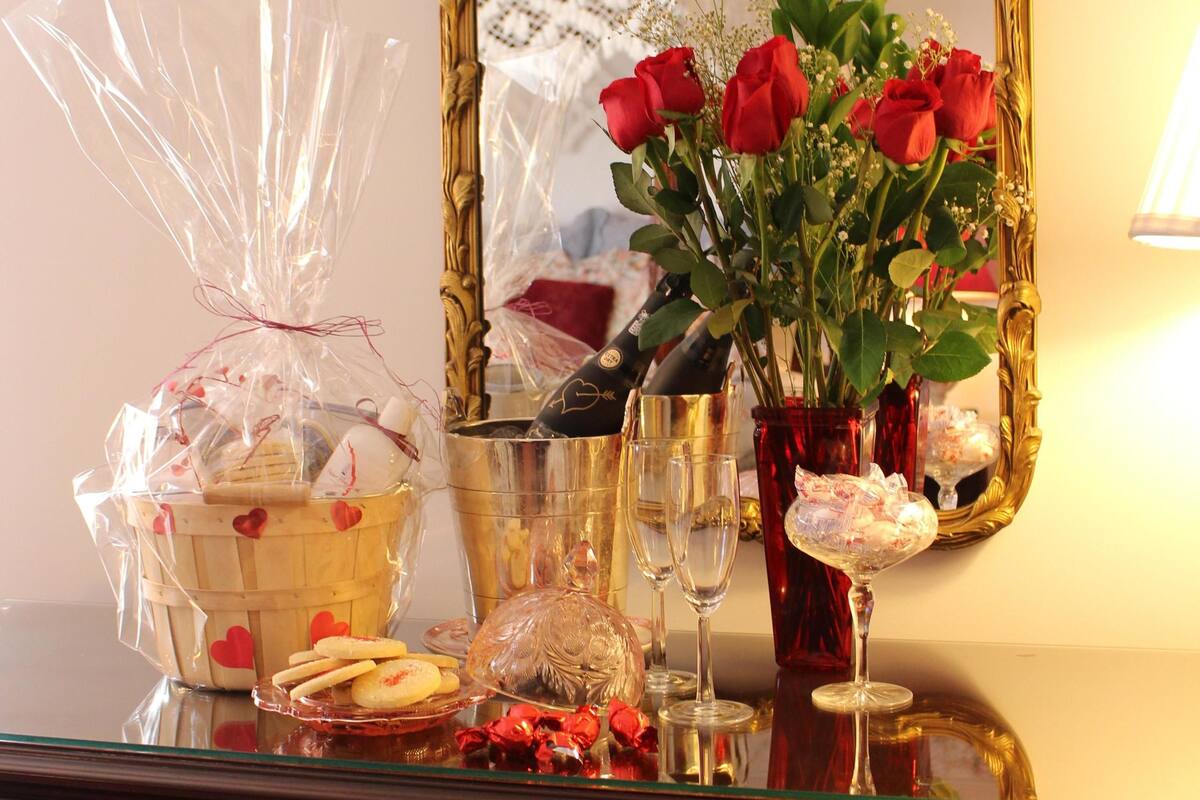 A wooden dresser with drawers, a mirror with an ornate frame, a vase with red roses, and various glassware and wrapped items on top.