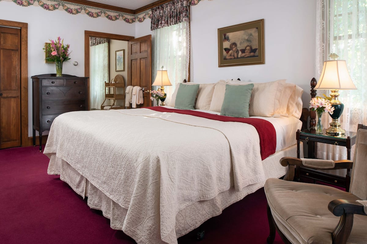 A bedroom with a large bed, a dresser, a chair, and a nightstand with a lamp.