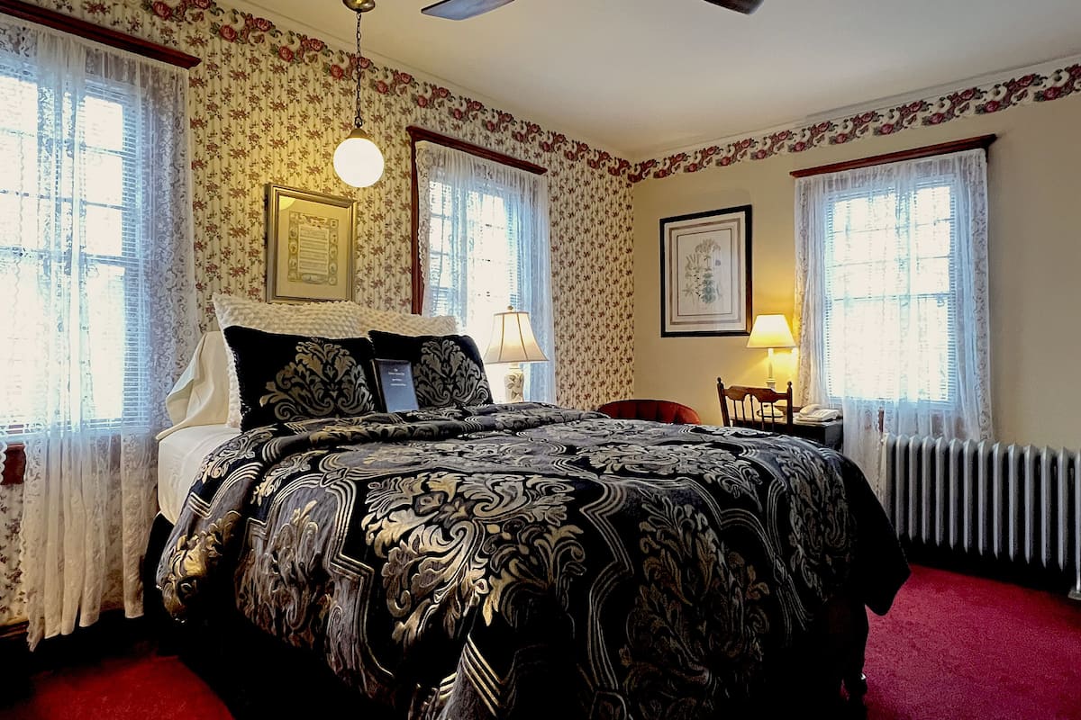 A bedroom with a large bed, two bedside tables, a chair, a ceiling fan, and a radiator.