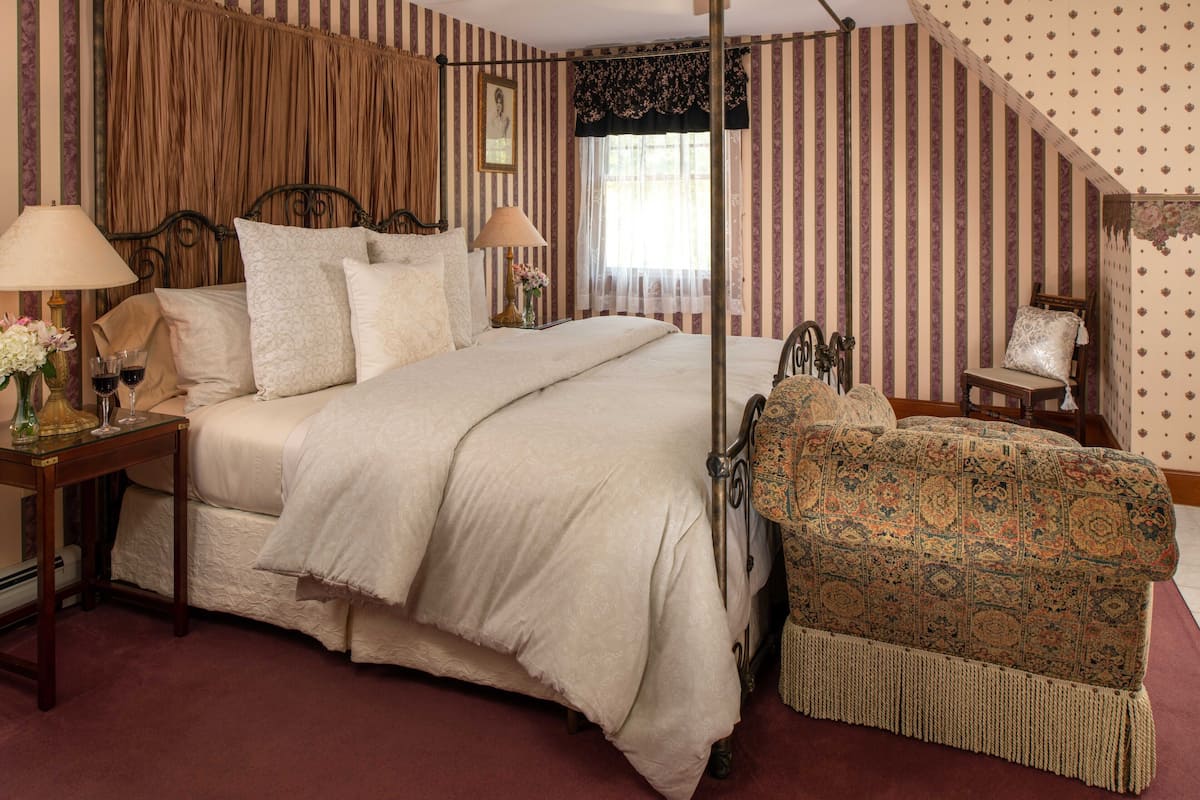 A bedroom with a large bed, two bedside tables with lamps, a chair, and a window with curtains.