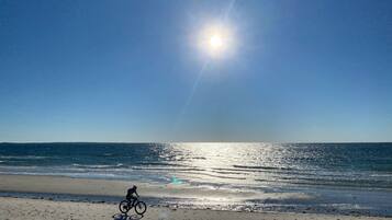 A beach with a cyclist, clear sky, and sun reflecting on the water.