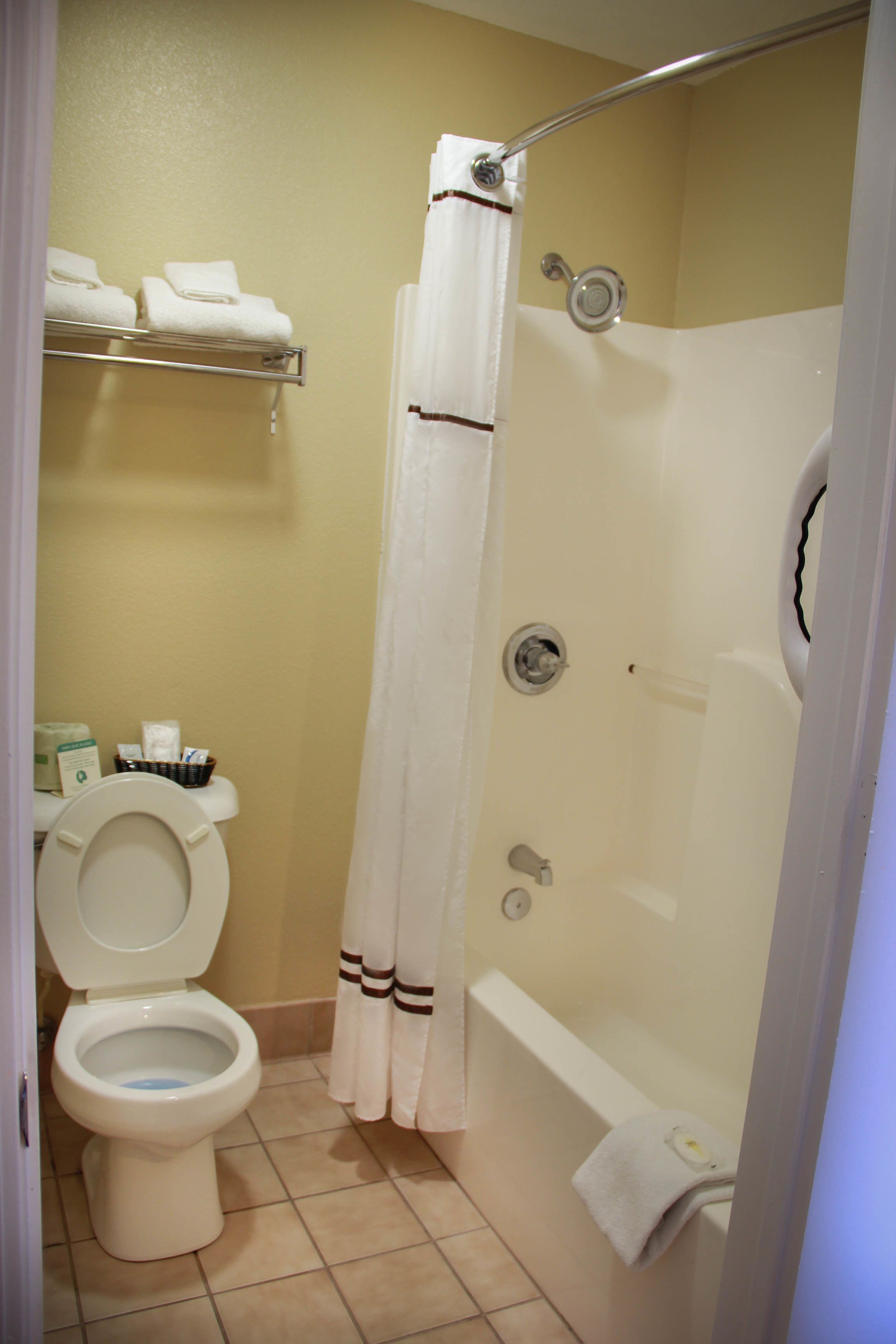 A bathroom with a toilet, a shower, and a bathtub. There are towels on a shelf and a curtain over the shower.