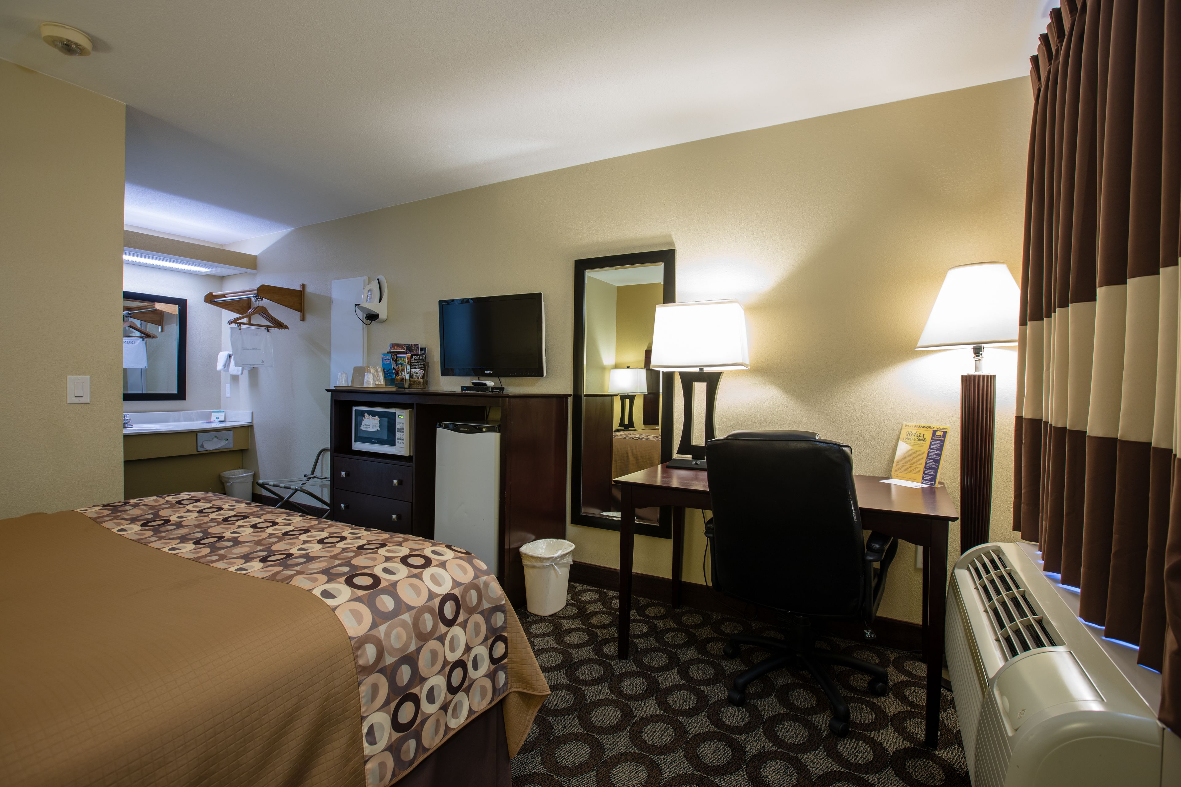 Habitación de hotel con cama, escritorio, silla, televisor y aire acondicionado.