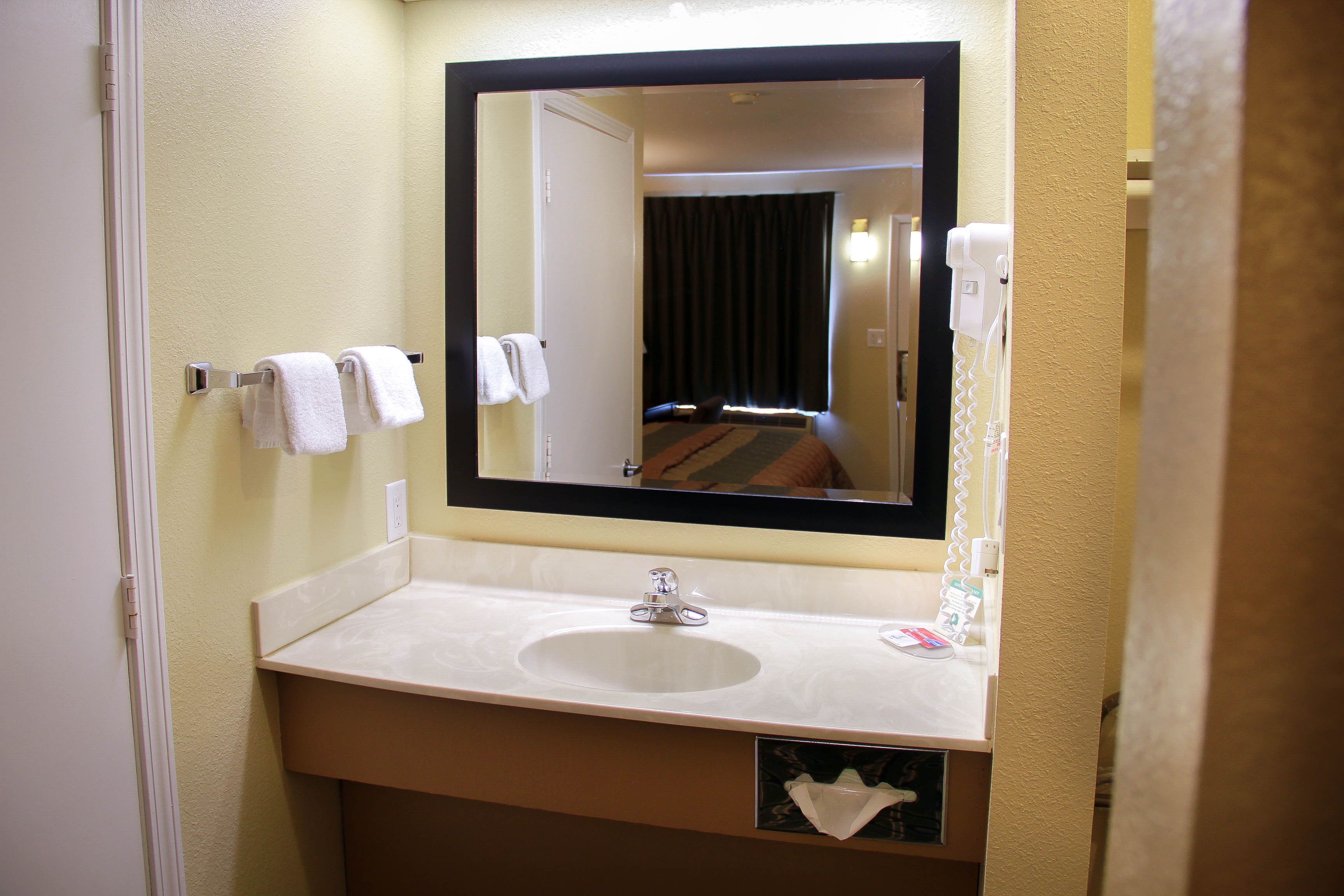 A hotel bathroom with a sink, mirror, and towel rack.