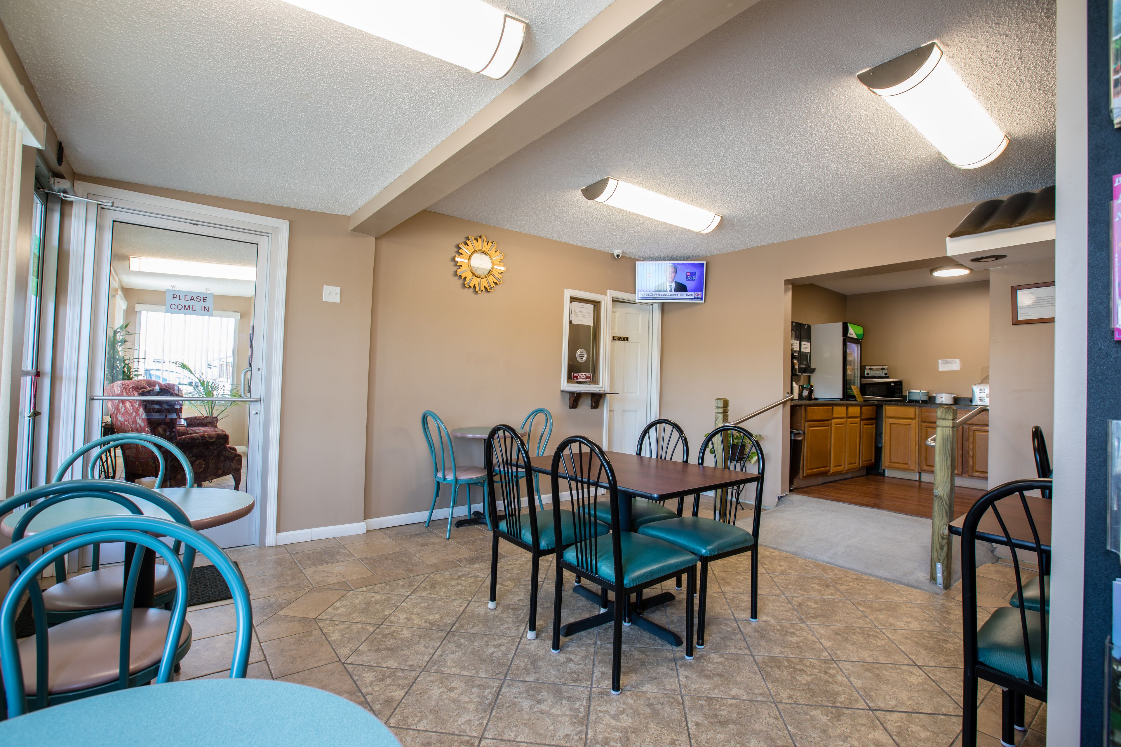 A dining area with teal chairs and a wooden table, a kitchen area with wooden cabinets, and a television mounted on the wall.