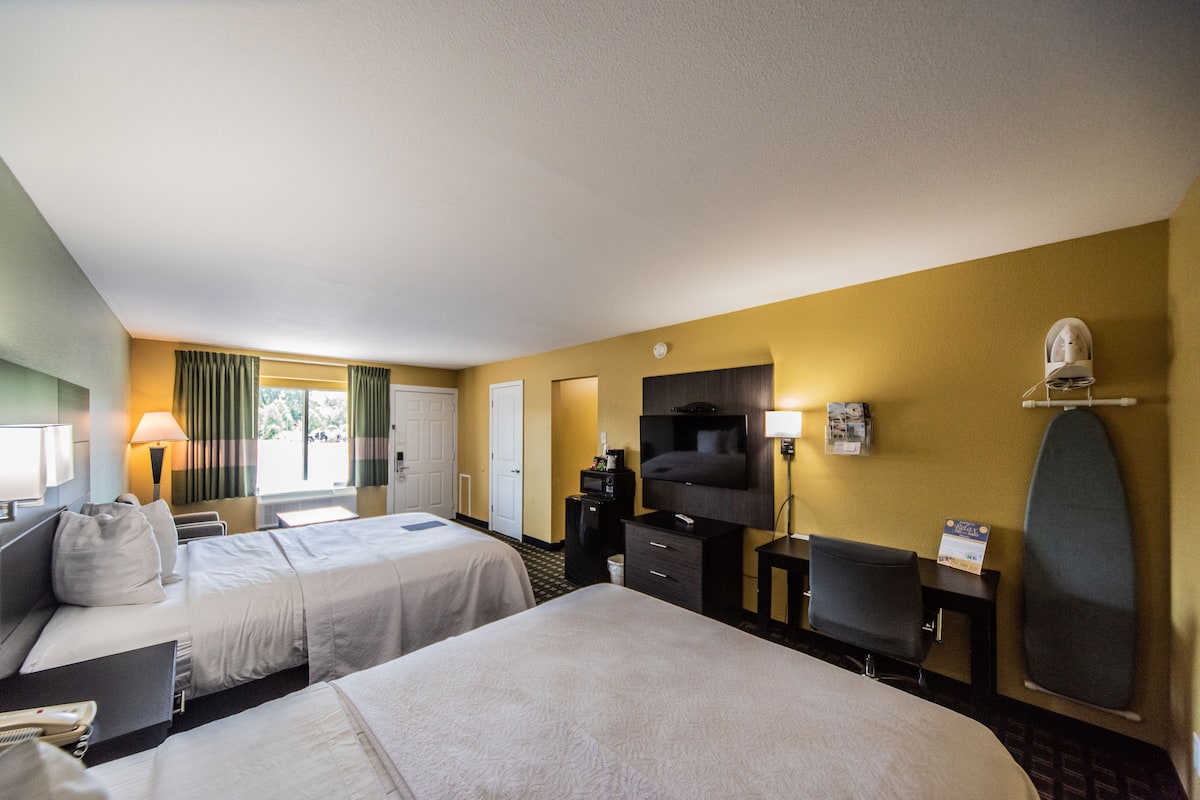 Quarto de hotel com duas camas, uma escrivaninha, uma televisão e um espelho.