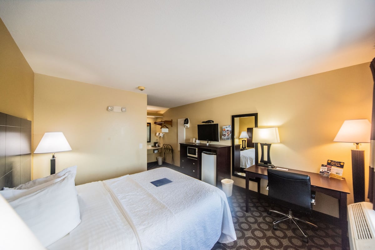 Quarto de hotel com cama, escrivaninha, cadeira e espelho.