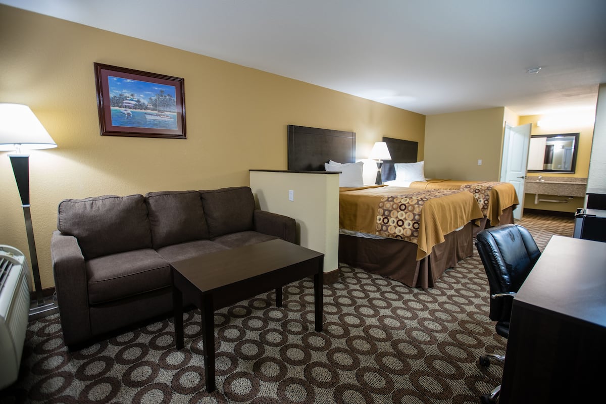 Quarto de hotel com sofá, mesa pequena, cama com colcha estampada, escrivaninha, cadeira, abajur, aquecedor, espelho e quadro na parede.