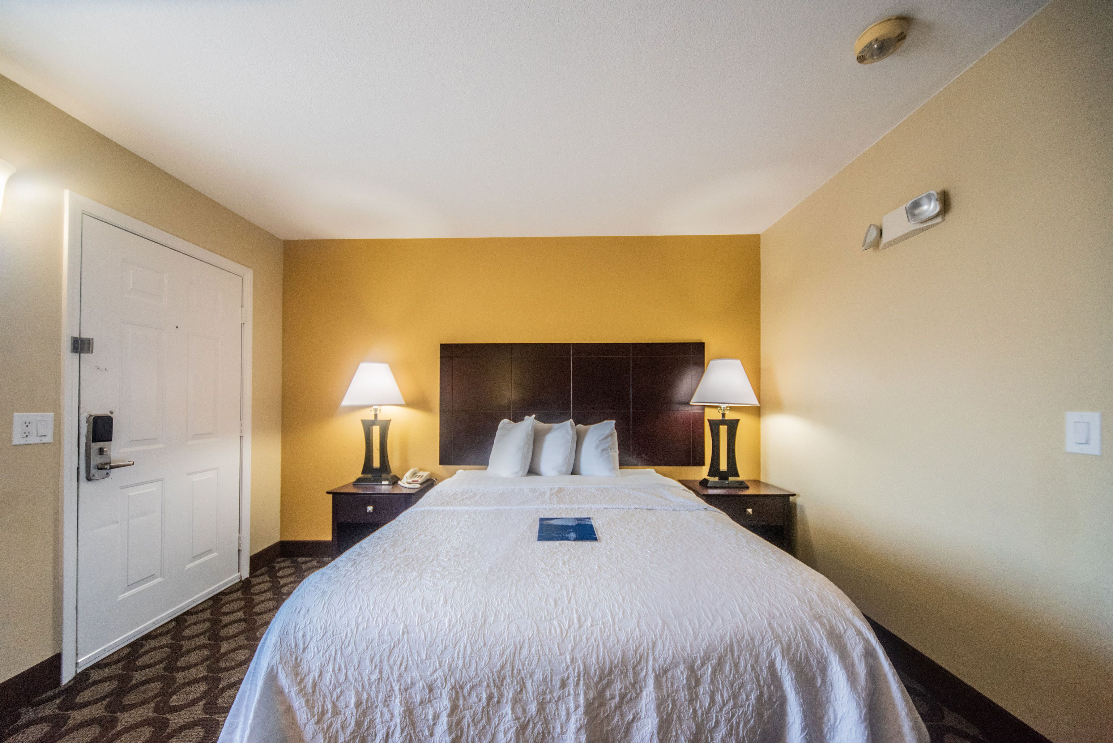 Une chambre d’hôtel avec un grand lit, deux tables de chevet avec des lampes, une porte et un luminaire fixé au mur.