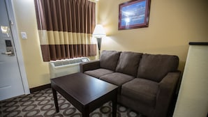 A hotel room with a brown sofa, a small table, a lamp, a picture on the wall, and a patterned carpet.