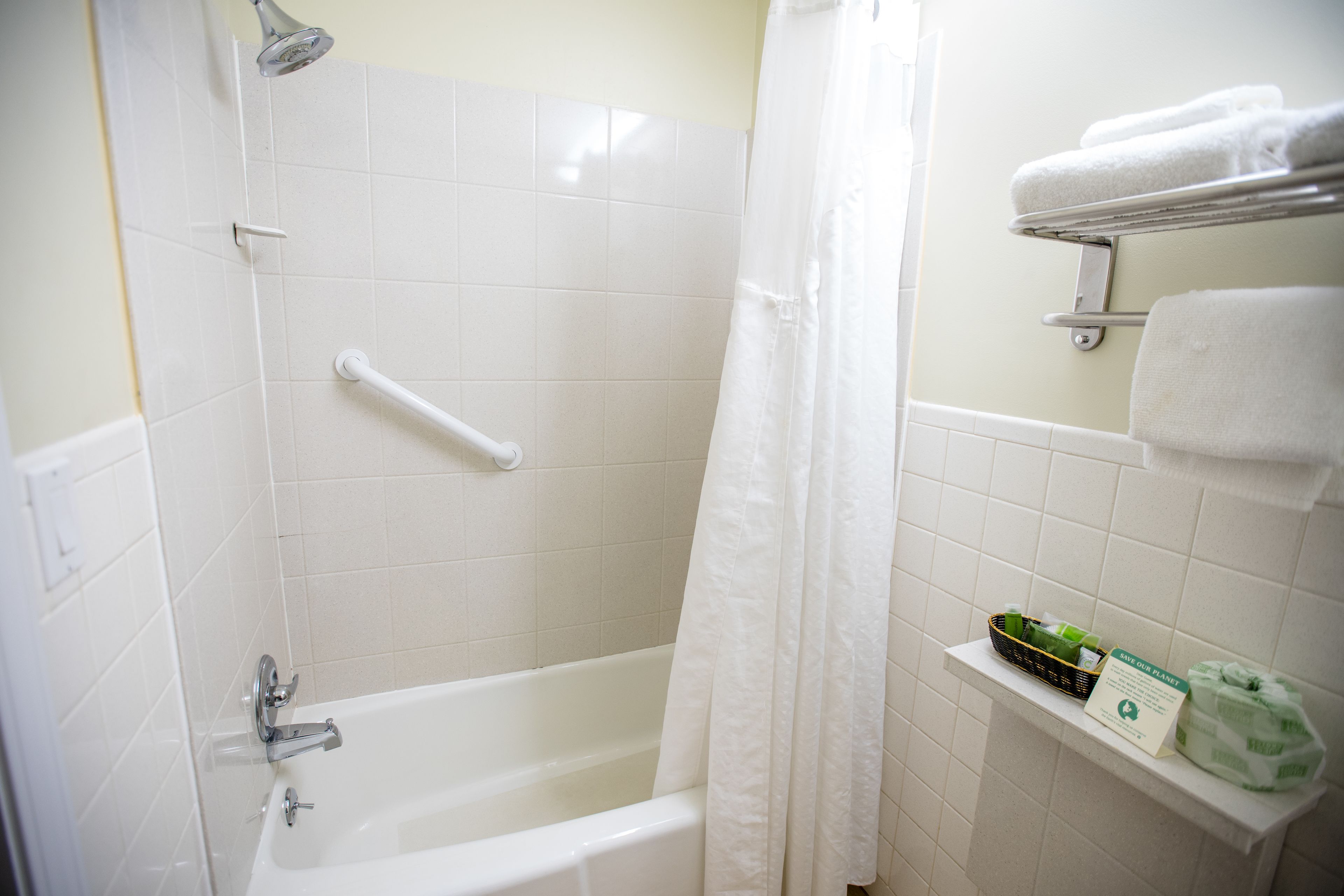A bathroom with a white bathtub, a shower curtain, a grab bar, and a shelf with toiletries.