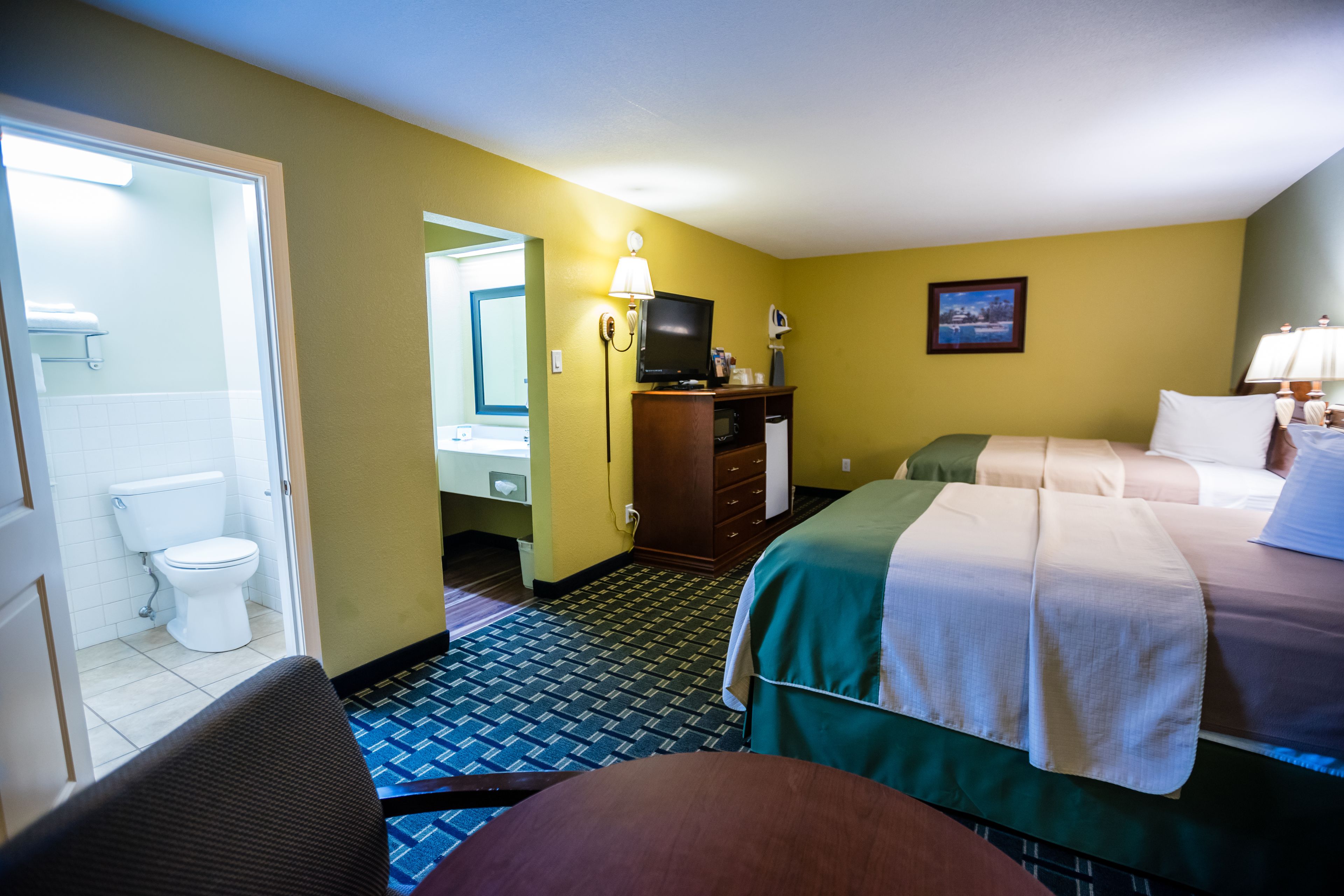 Une chambre d’hôtel comprenant un lit, un bureau, une chaise, une télévision, une salle de bain avec des toilettes et un miroir.