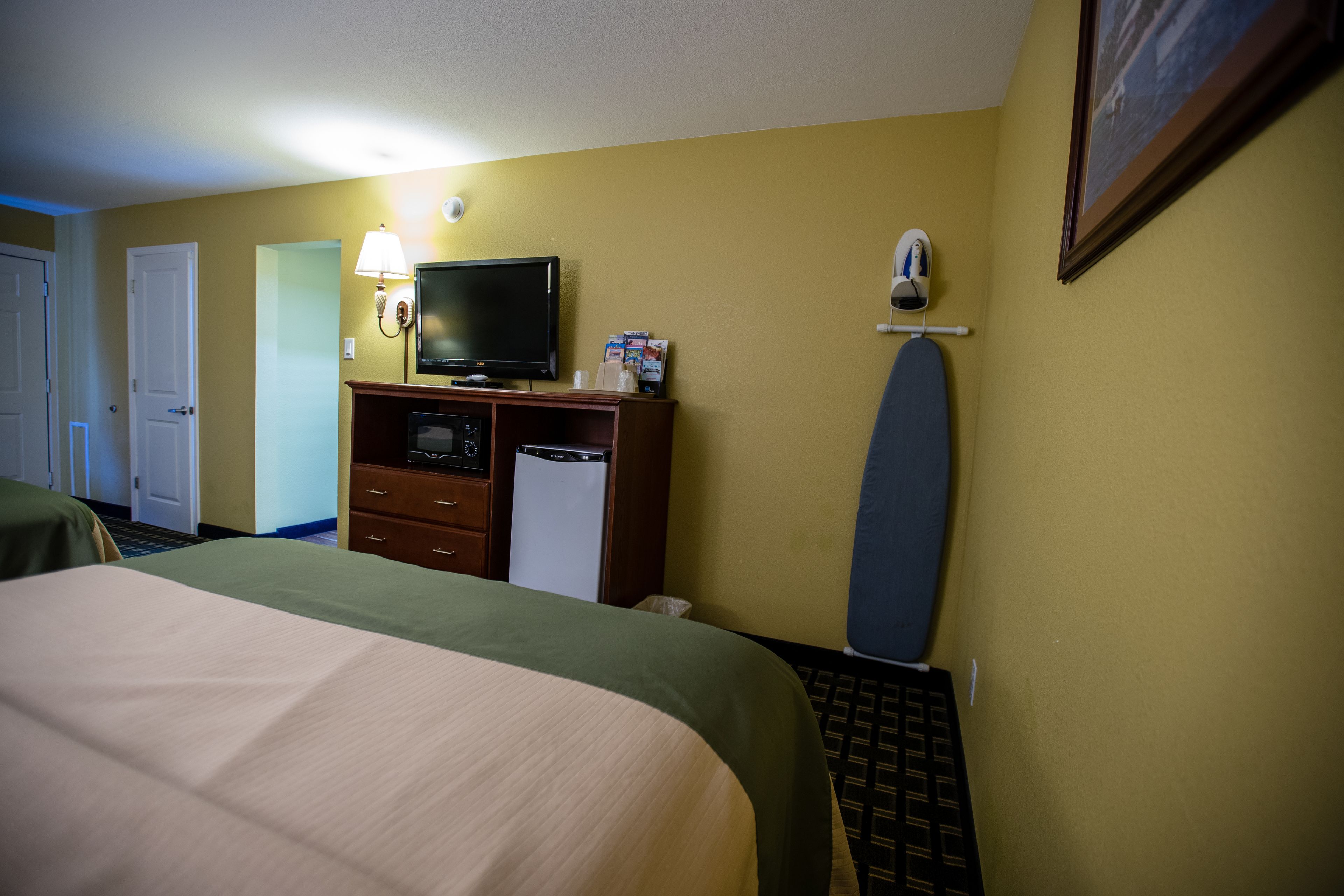 A hotel room with a bed, a desk with a television, a microwave, and a small refrigerator.
