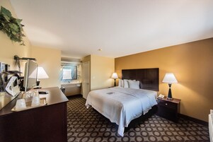 Habitación de hotel con cama, dos lámparas de noche, un escritorio con lámpara, teléfono y una bandeja con vasos.