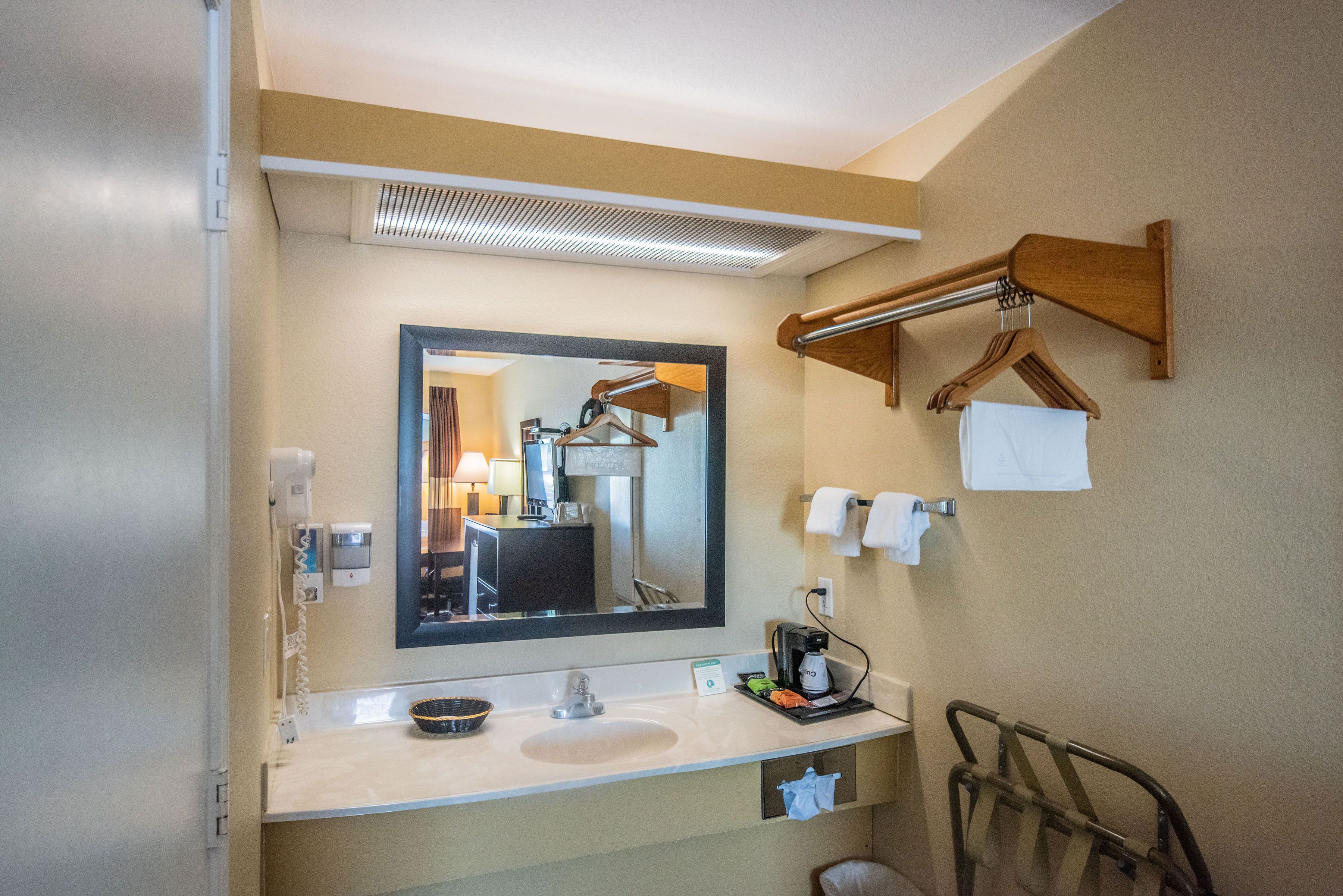 A hotel bathroom with a sink, mirror, towel rack, and a towel dispenser.